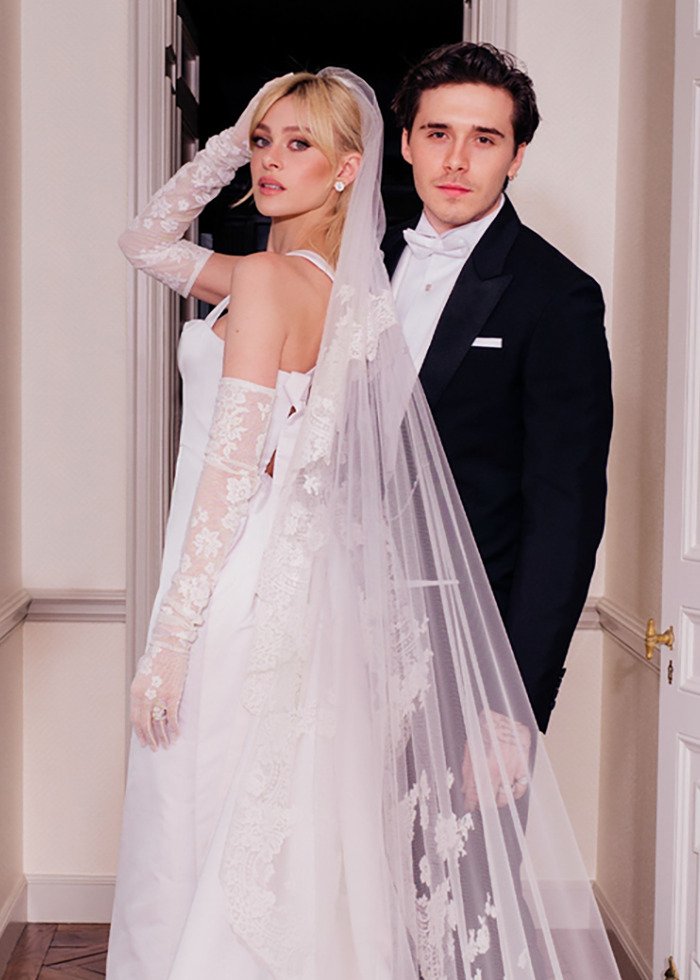 Bride in lace gloves and veil poses with groom in tuxedo at wedding, capturing the moment amid Beckham family fallout.