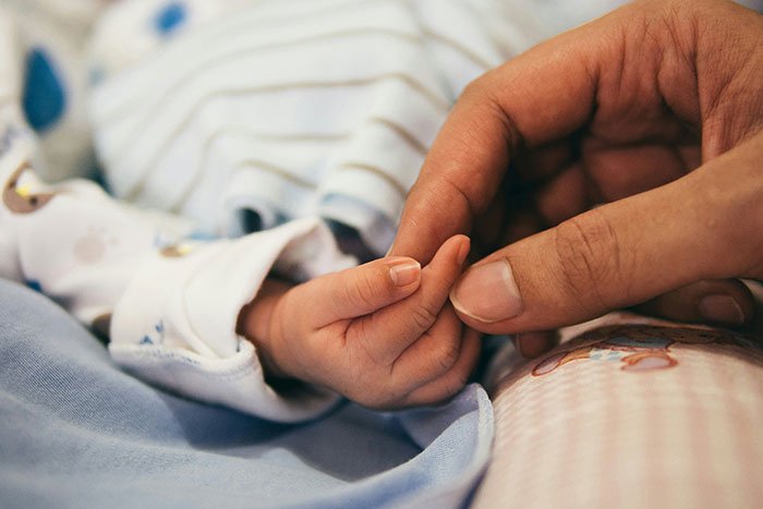 Close-up of newborn baby holding adult finger, highlighting emotional bond after woman gives birth in friends' car.