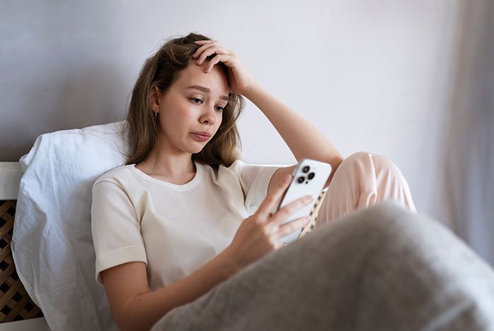 Young woman looking confused while using her phone, reflecting feelings after giving birth in friends' car and being ignored.
