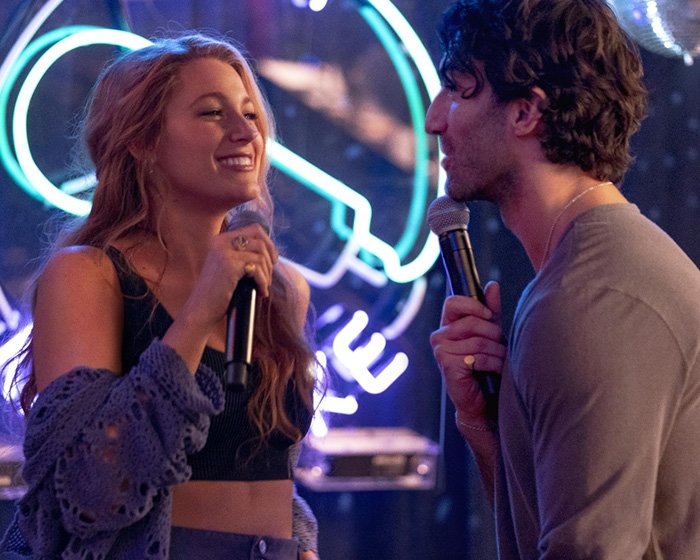 Blake Lively and a man holding microphones in a lively setting hint at Taylor Swift's wedding to Travis Kelce rumors.