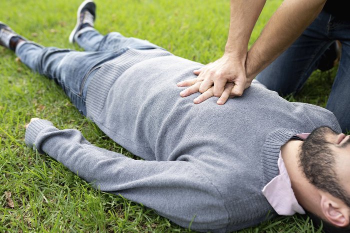 Person performing CPR on a man lying on grass, illustrating the impact of SOS code on rescue missions.
