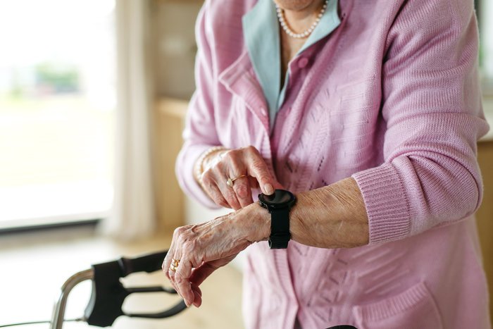 Elderly woman in pink sweater using a smart watch, highlighting SOS technology in modern rescue missions.