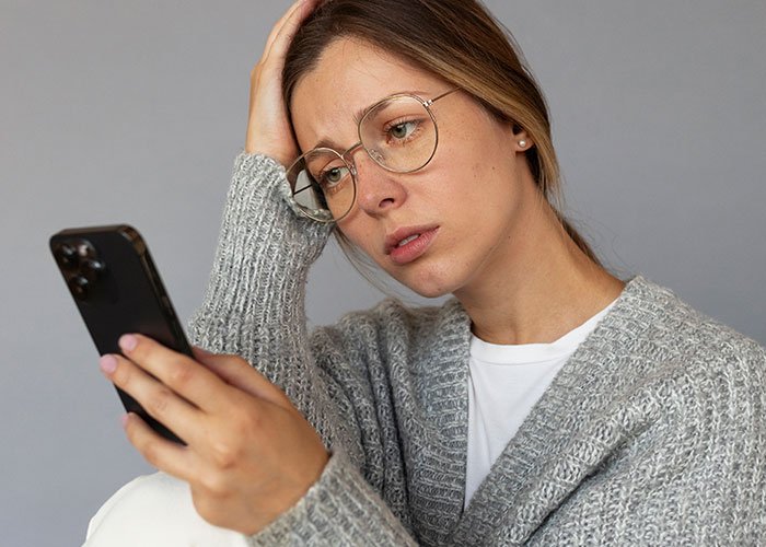 Woman in a gray sweater looking upset while holding a phone, reflecting frustration over a rejected baby shower idea.