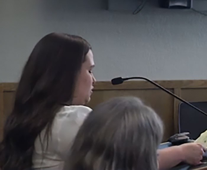 Young woman speaking into a microphone during a formal setting, related to bold texts from teacher to student.