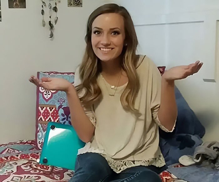 Young woman sitting on bed with laptop, smiling and raising hands, representing bold texts from teacher to student incident.
