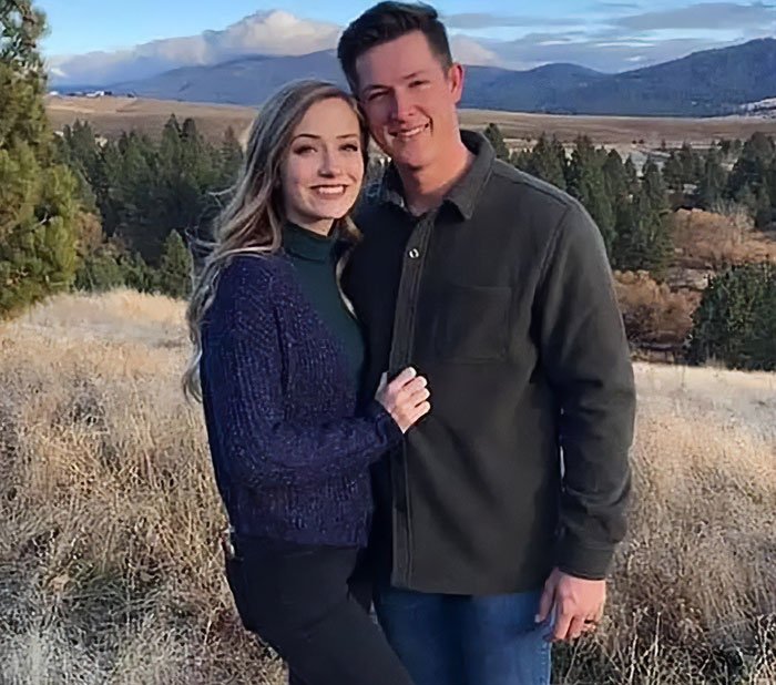 Couple posing outdoors with scenic mountain and forest background during a casual fall day.