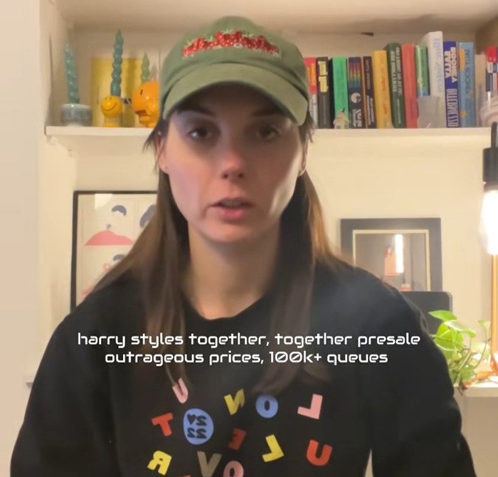 Young woman in casual cap and sweatshirt discussing Harry Styles new tour tickets with outrage over prices and presale queues.
