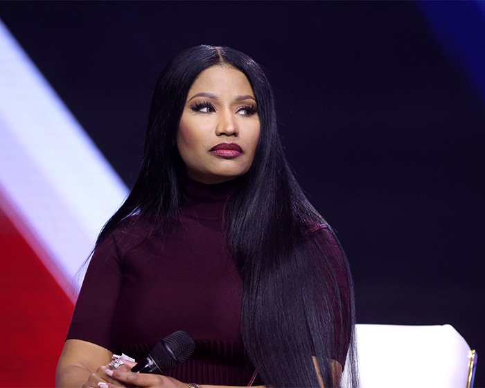 Nicki Minaj holding a microphone, wearing a dark top, looking to the side during a public event after Ariana Grande snub news.