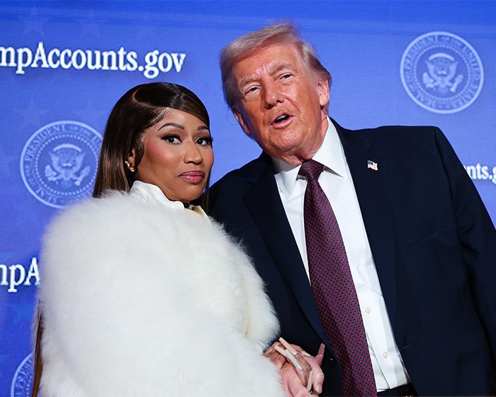 Nicki Minaj wearing white fur coat posing with Donald Trump at a political event with blue backdrop and seal logos.