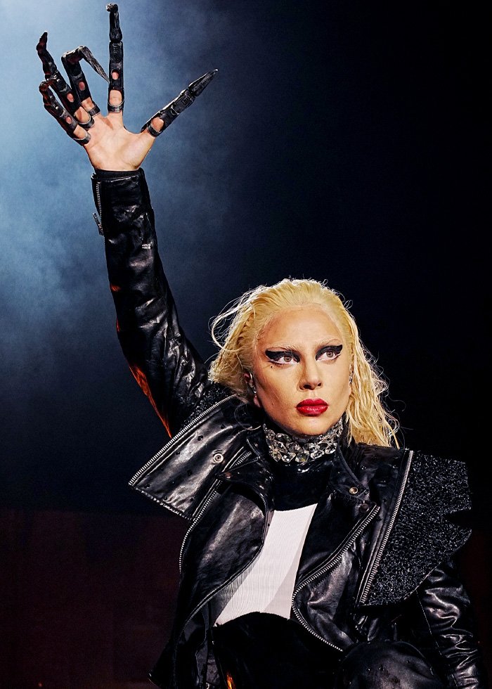 Lady Gaga in dramatic black outfit and glove raising hand during concert delivering bold ICE speech on stage.