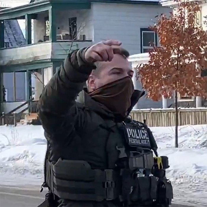 Police officer in tactical gear and face covering outside near houses and snow, related to bold ICE speech incident.