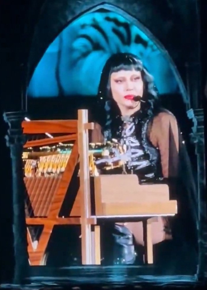 Lady Gaga performing at concert, wearing headset microphone and playing piano during bold ICE speech.