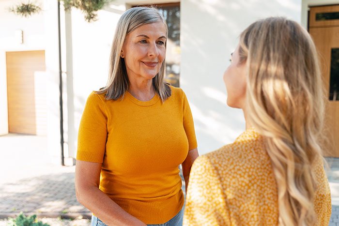 Middle-aged mom in orange top talking to daughter outdoors about DNA test concerns and family matters.