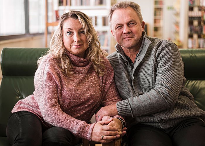 Middle-aged woman and man sitting closely on a couch, holding hands, considering a DNA test with mixed emotions.