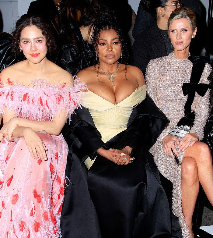 Taraji P. Henson seated between two women, wearing a yellow dress and black coat, with fans discussing face changes.