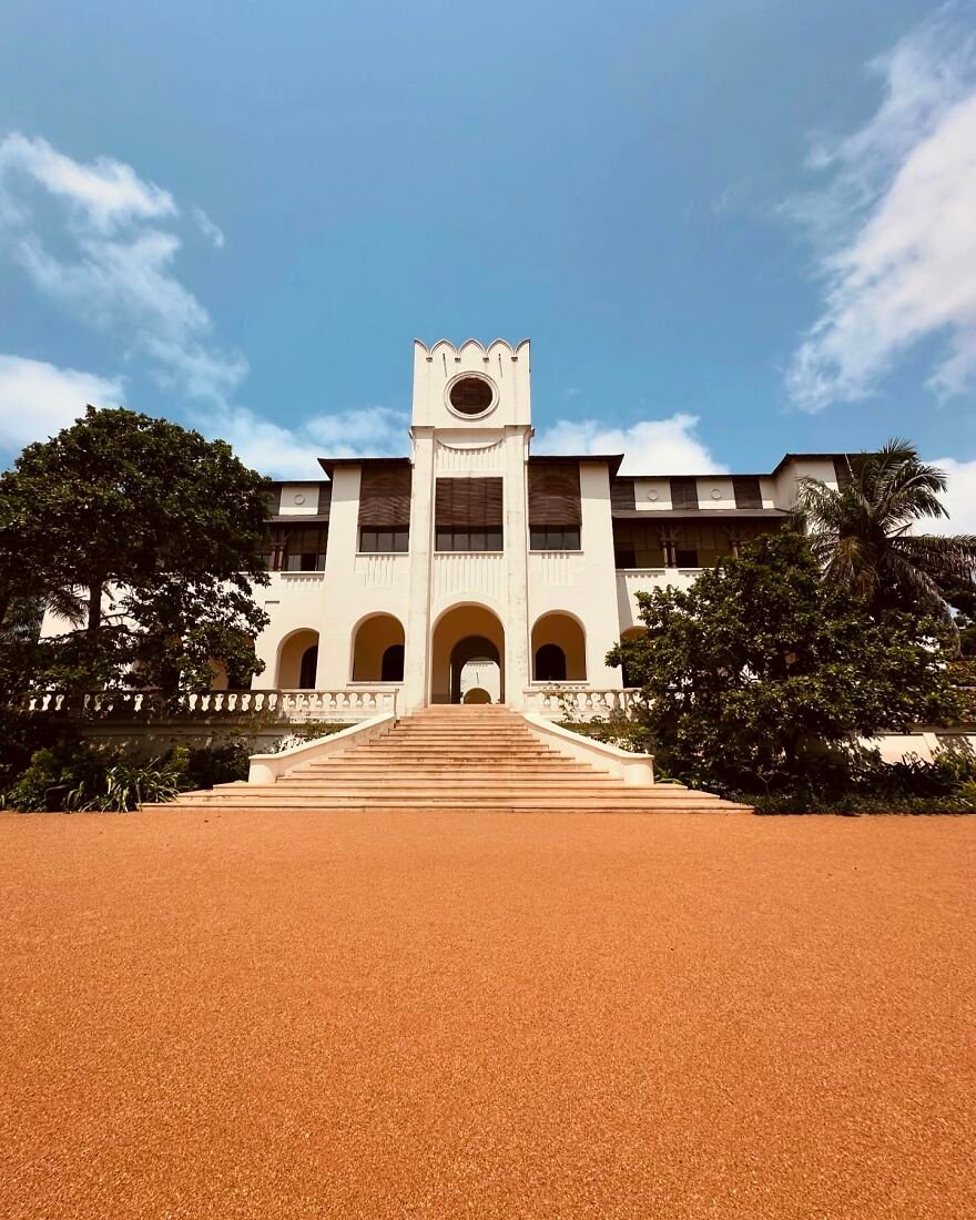 Colonial-style building with wide stairs surrounded by greenery under a blue sky representing paid leave in global nations.