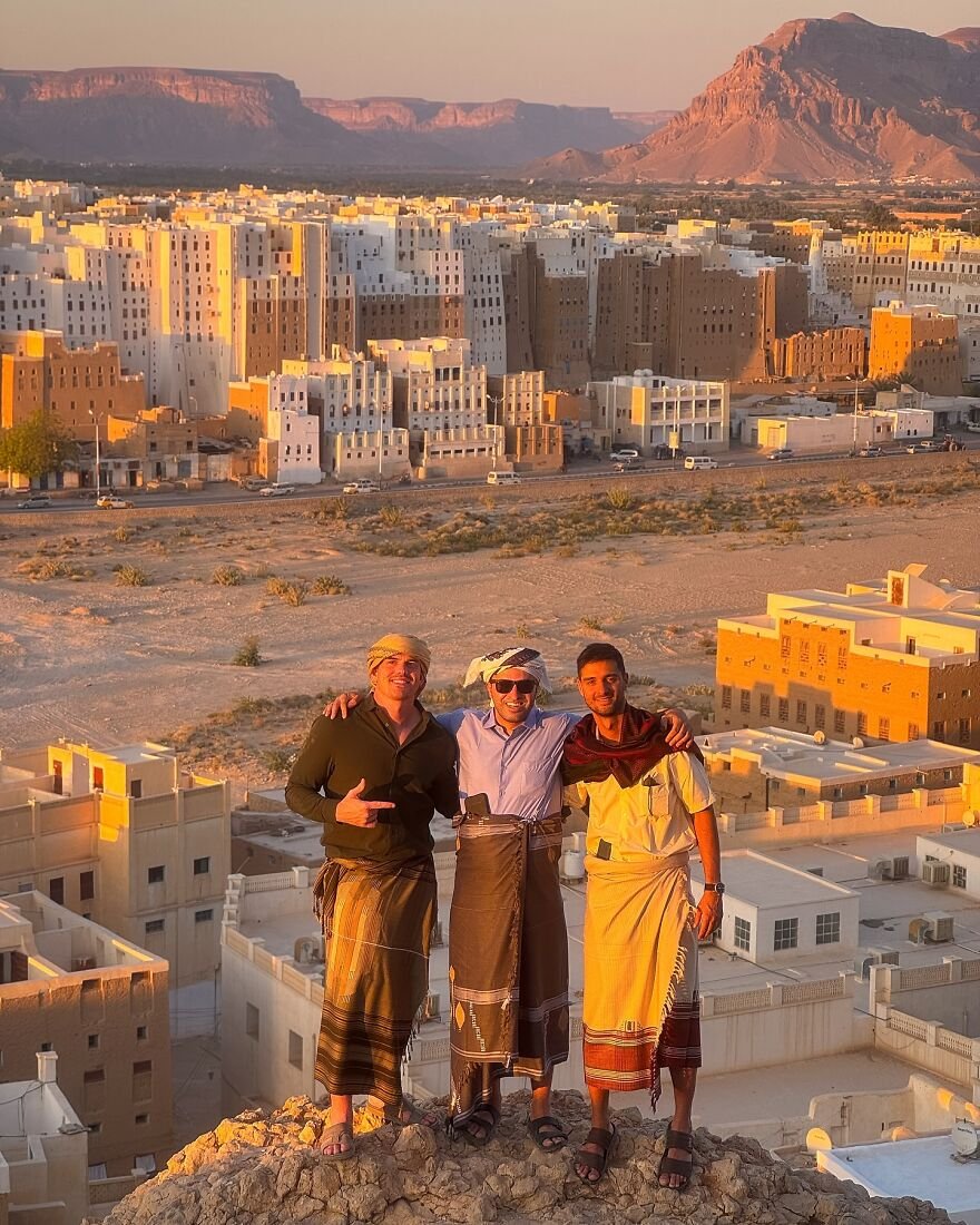 Three men wearing traditional clothing pose happily overlooking a cityscape, illustrating nations setting new global paid leave standards.