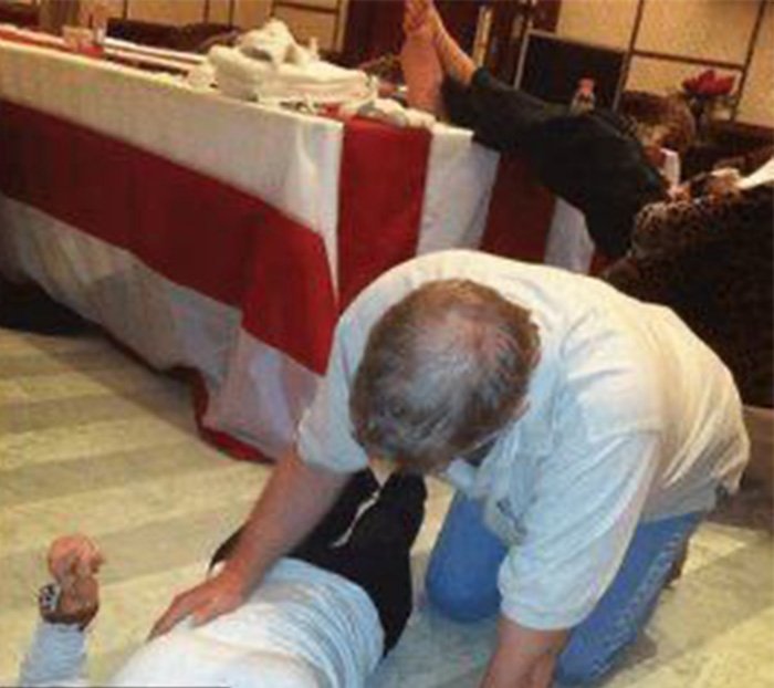 Disturbing images related to Prince Andrew show a man lying on the floor with another person leaning over him indoors.