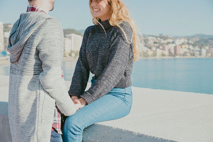 Couple holding hands outdoors by water with woman smiling, illustrating SAHM wife and financial problems theme.