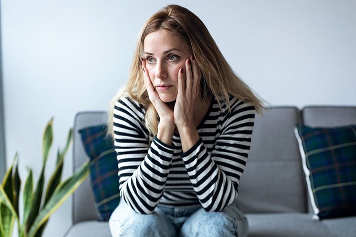 Worried stay-at-home mom sitting on sofa, reflecting on financial problems and husband blaming her for the issues.