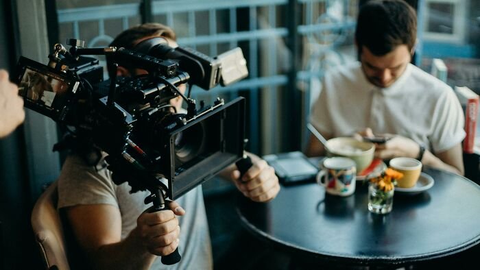 Filmmaker operating a professional camera in a cafe setting capturing scenes for films that got lost in translation.
