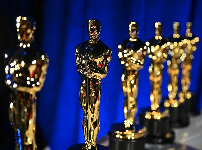 Shiny golden Oscar statuettes lined up against a blue background for Academy 2026 Oscar nominations event.