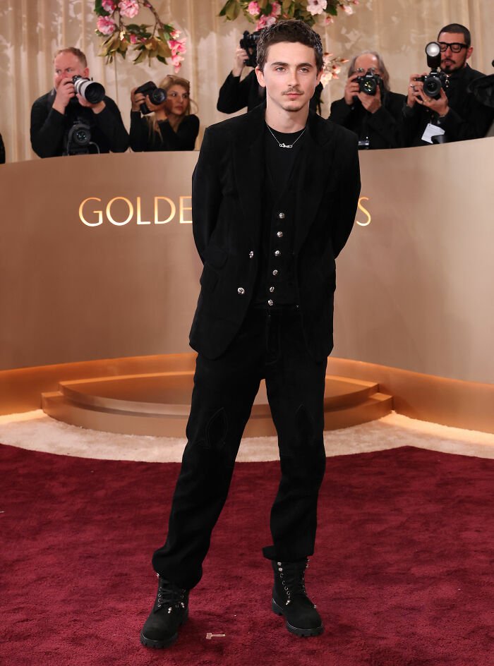 Timothée Chalamet on the red carpet at the Golden Globes event, dressed in black with photographers in the background.