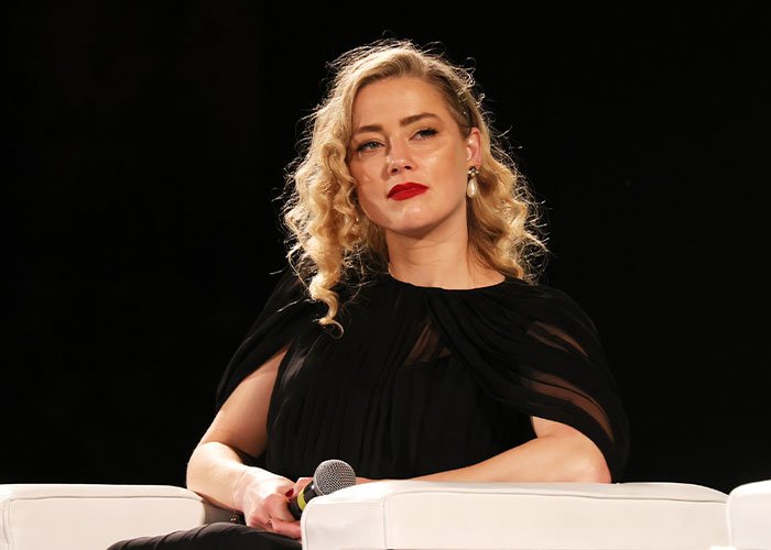 Amber Heard sitting on stage holding a microphone during a discussion about defamation suits and the Depp trial.