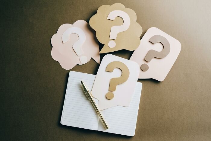 Notebook and pen surrounded by speech-bubble question marks representing commonly confused word pairs.