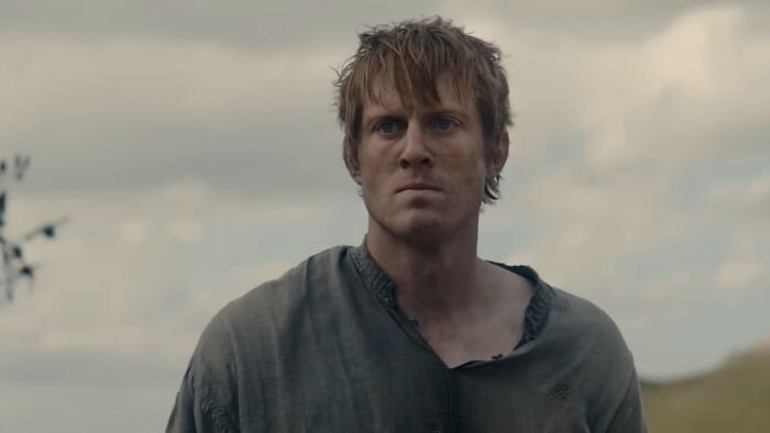 Young man with determined expression in medieval clothing outdoors, related to George RR Martin and A Knight of the Seven Kingdoms.