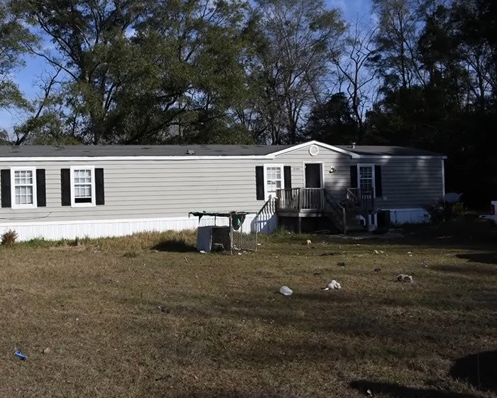 Exterior view of an isolated mobile home with yard litter, linked to a girl abandoned for a year in a devastating situation.
