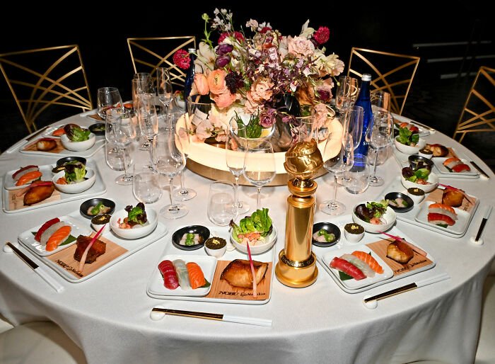 Golden Globes food presentation with sushi plates, salads, a gold trophy centerpiece, and floral arrangement on a round table.
