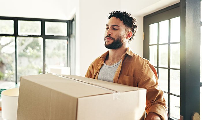 Man moving large box into home, representing man accidentally moves in next door to former friend conflict story.