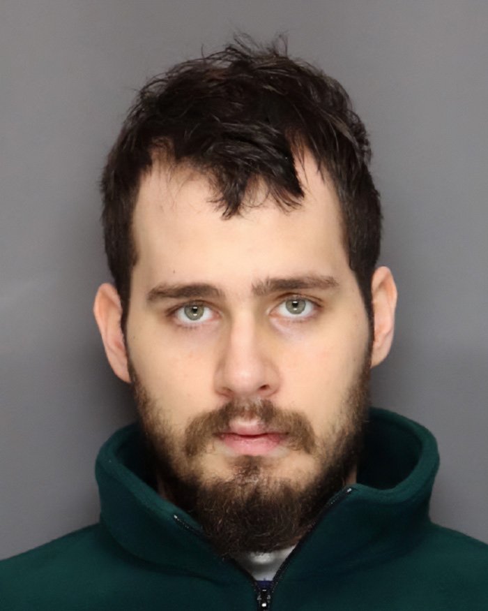 Man with dark hair and beard in a green jacket facing camera in a mugshot related to pregnant sister homicide charges.