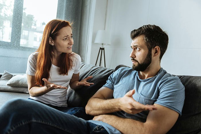 Man and woman having a tense conversation on couch, reflecting a man failing to buy his girlfriend Christmas presents.
