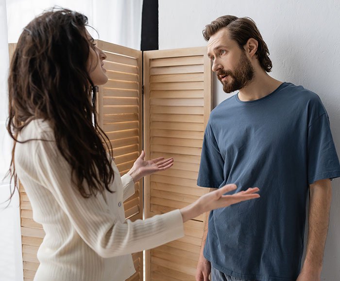 Man and woman having a tense conversation, illustrating a man trying to blame wife for no slacks on business trip.