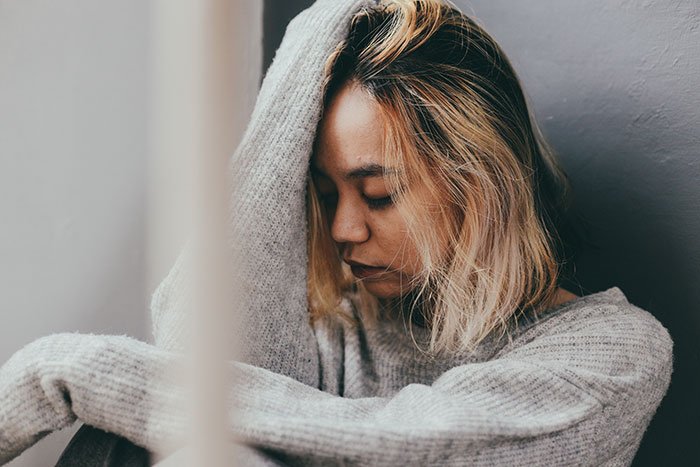 Young woman with blonde hair in a gray sweater looks contemplative, reflecting on DNA test conflict with her mom.