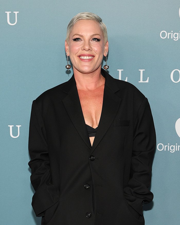 Pink smiling at an event, wearing a black blazer and earrings, after spending New Year’s Eve alone in hospital.