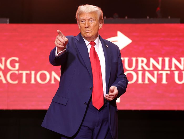 Former President Trump in a navy suit and red tie pointing, highlighting changes in Trump’s hair color by a professional stylist.