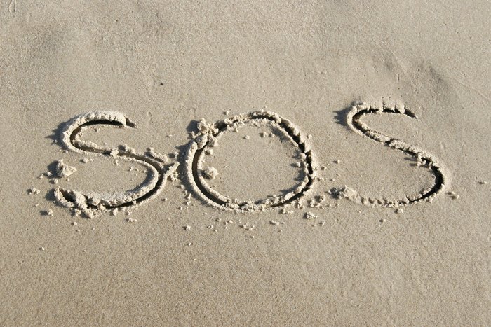 SOS written in sand on a beach symbolizing the simple code used in rescue missions worldwide for emergencies.