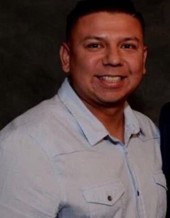 Smiling man in a light blue shirt against a dark background, related to teacher’s life ends after diary affair discovery.