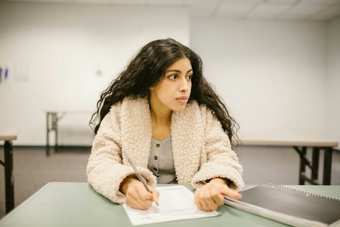 Young woman focused on testing her vocabulary skills in a language quiz while sitting at a desk with papers and notebook.