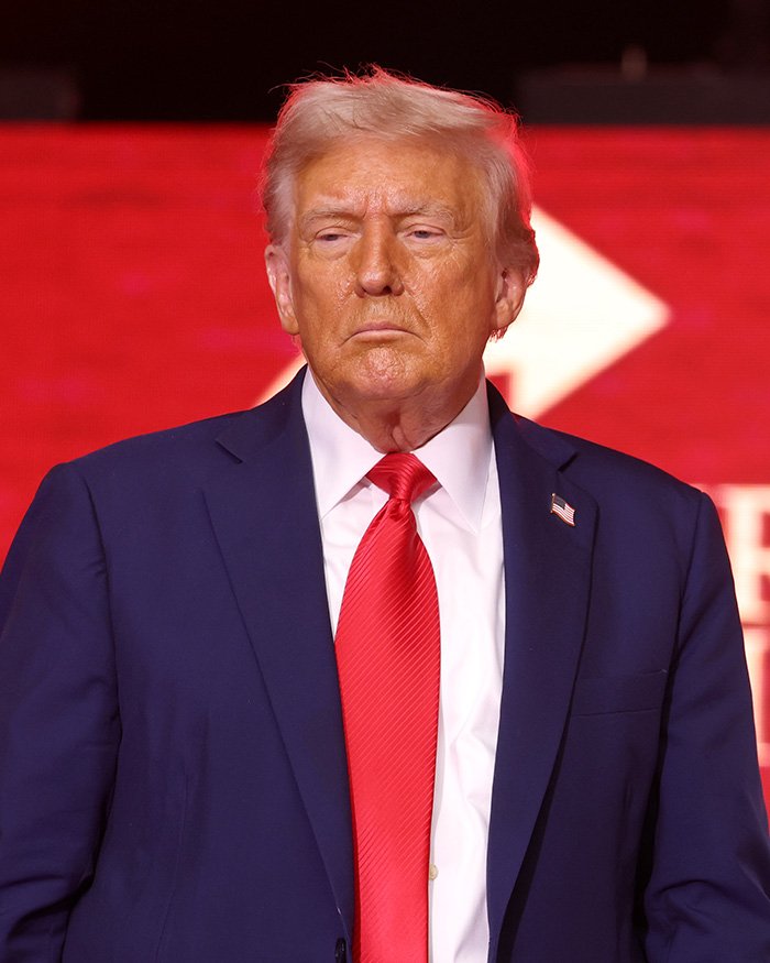 Donald Trump in a dark suit and red tie with a serious expression as health speculation and doctor concerns arise about droopy face.