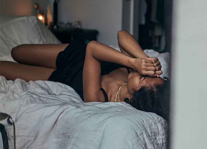 Woman lying on bed with hands covering face, reflecting defeat and karma after affair partner leaves her.