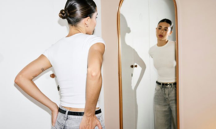 Woman looking in a mirror, reflecting on body image and reacting to coworker skinny-shaming and body positivity conflict.