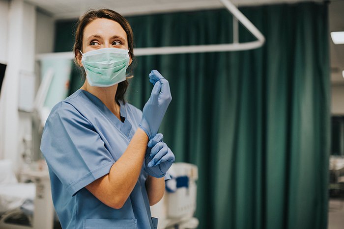 Woman in medical scrubs wearing a mask and putting on gloves, portraying a healthcare professional in a hospital setting.