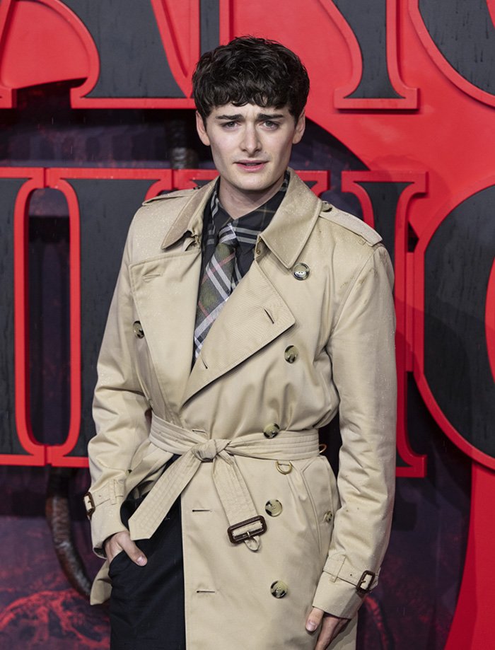 Noah Schnapp at an event, wearing a beige trench coat and patterned tie, relating to Stranger Things star news.