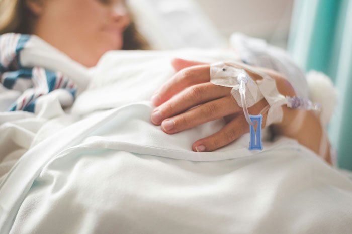 Woman resting in hospital bed with IV line, depicting struggle over inheritance and family conflict after husband's death