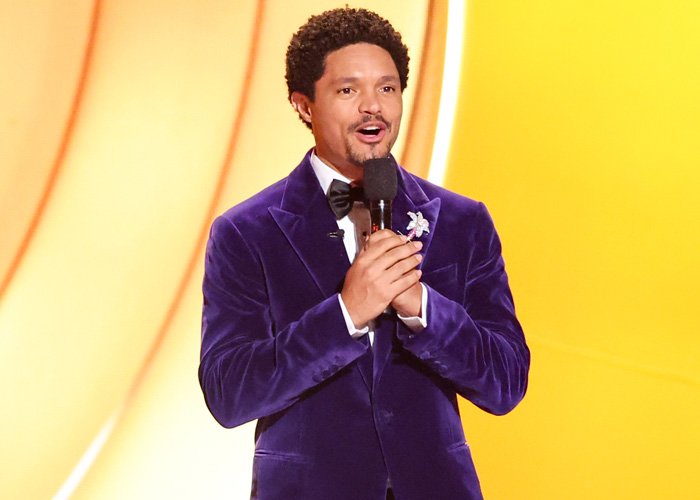 Trevor Noah speaking on stage in a purple velvet jacket, illustrating body language expert analysis of tense behavior.