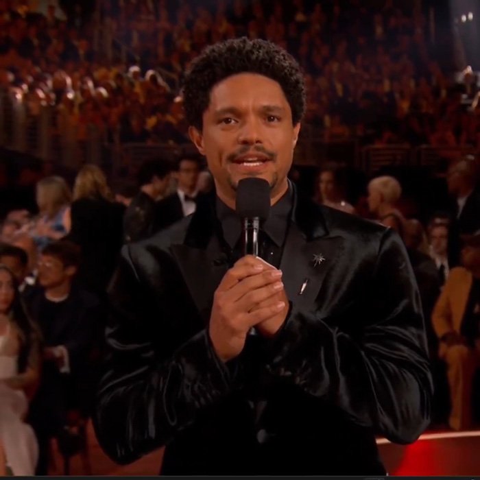 Trevor Noah speaking at the Grammys event, wearing a black suit, sparking wild theories with his bizarre statement.